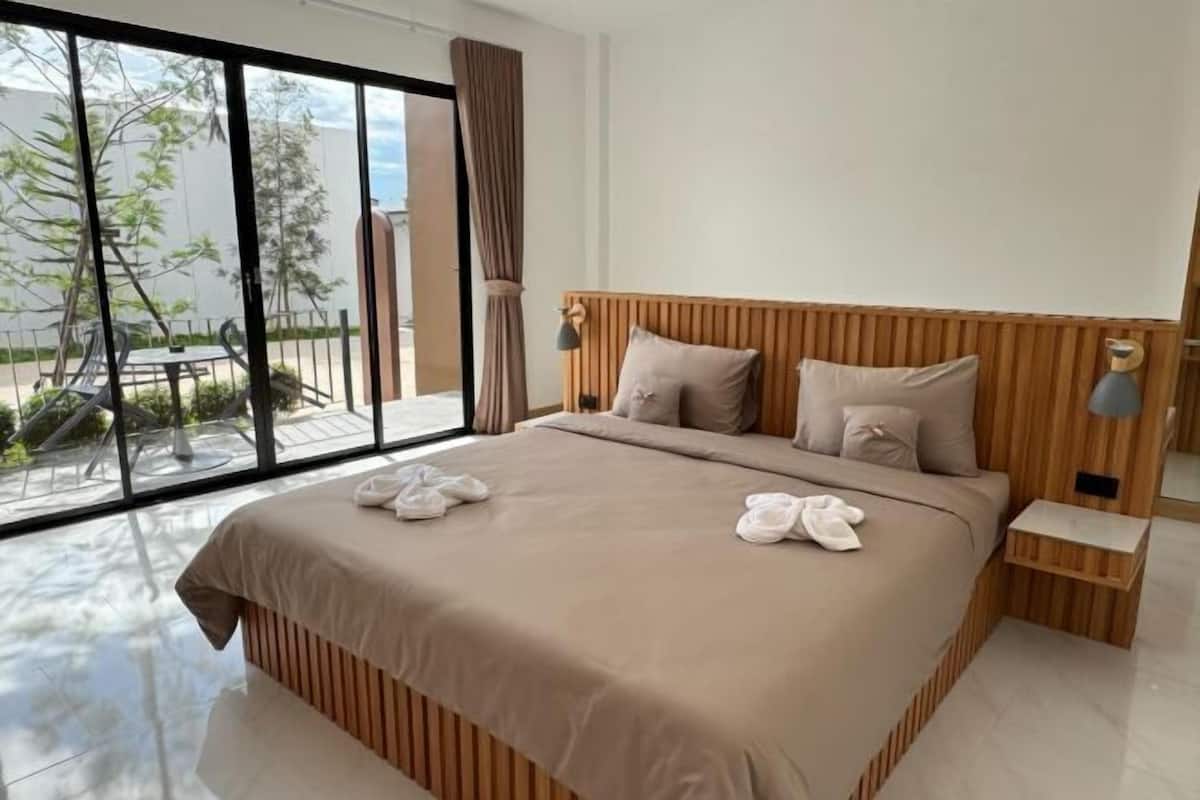 Ein modernes Hotelzimmer mit einem großen Bett, einem hölzernen Kopfteil und Blick ins Freie durch große Fenster.