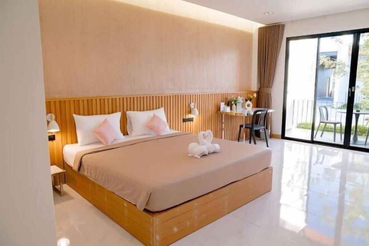 Ein modernes Hotelzimmer mit einem großen Bett, einem kleinen Schreibtisch und Blick ins Freie durch eine Schiebetür.