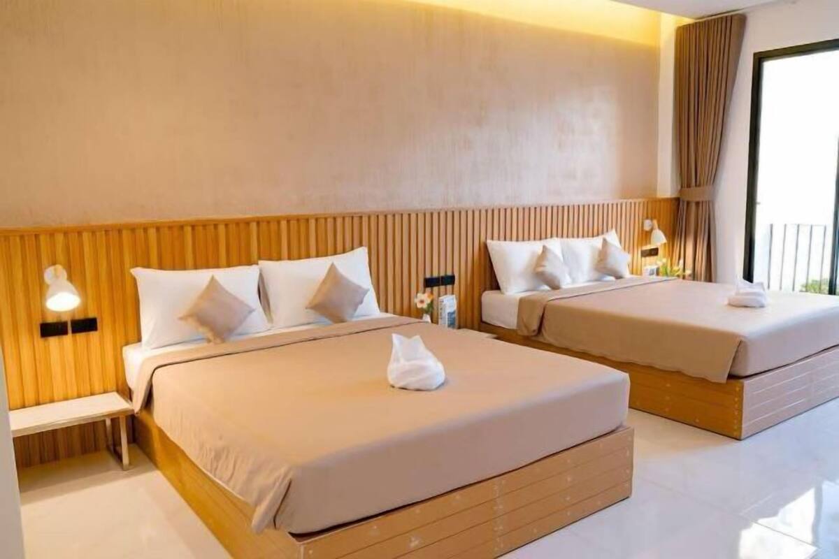 Ein Hotelzimmer mit zwei Betten, Holz-Kopfteilen, Nachttischen und einem großen Fenster mit Vorhängen.