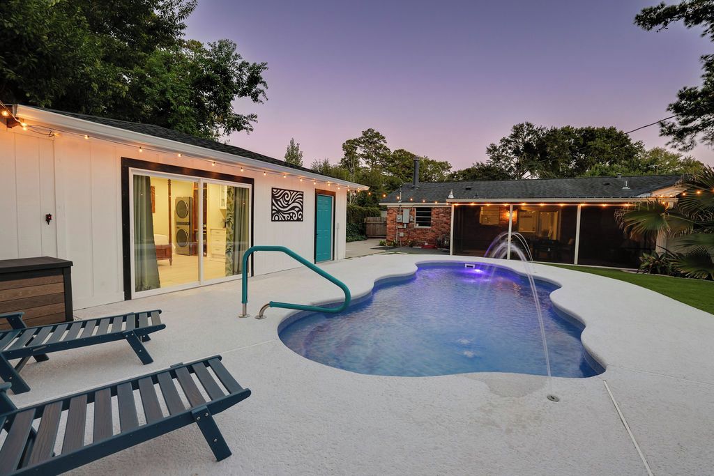 A backyard with a swimming pool, lounge chairs, and a covered patio area.