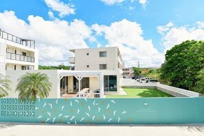 Un edificio moderno con techo plano, un balcón y un pequeño jardín.