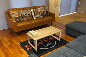 A living room with a brown leather sofa, a coffee table, and a grey couch. - HOTEL YANBARUNIA (Nago)