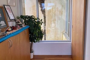 A room with a wooden cabinet, a potted plant, and a window with a view of a tree. - HOTEL YANBARUNIA (Nago)