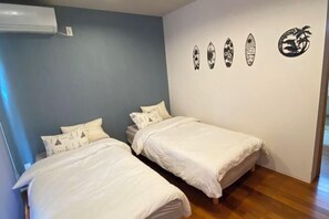 A room with two single beds, a wall-mounted air conditioner, and four surfboard-shaped wall art pieces. - HOTEL YANBARUNIA (Nago)
