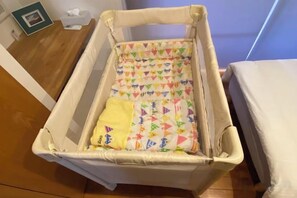 A crib with a colorful quilt, a white mattress, and a wooden floor. - HOTEL YANBARUNIA (Nago)