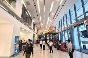 A spacious indoor area with a high ceiling, large windows, and a seating area with a red chair. - Luxury Family Summer Suite KLCC 5 min walk 1BR by Amna (Kuala Lumpur)