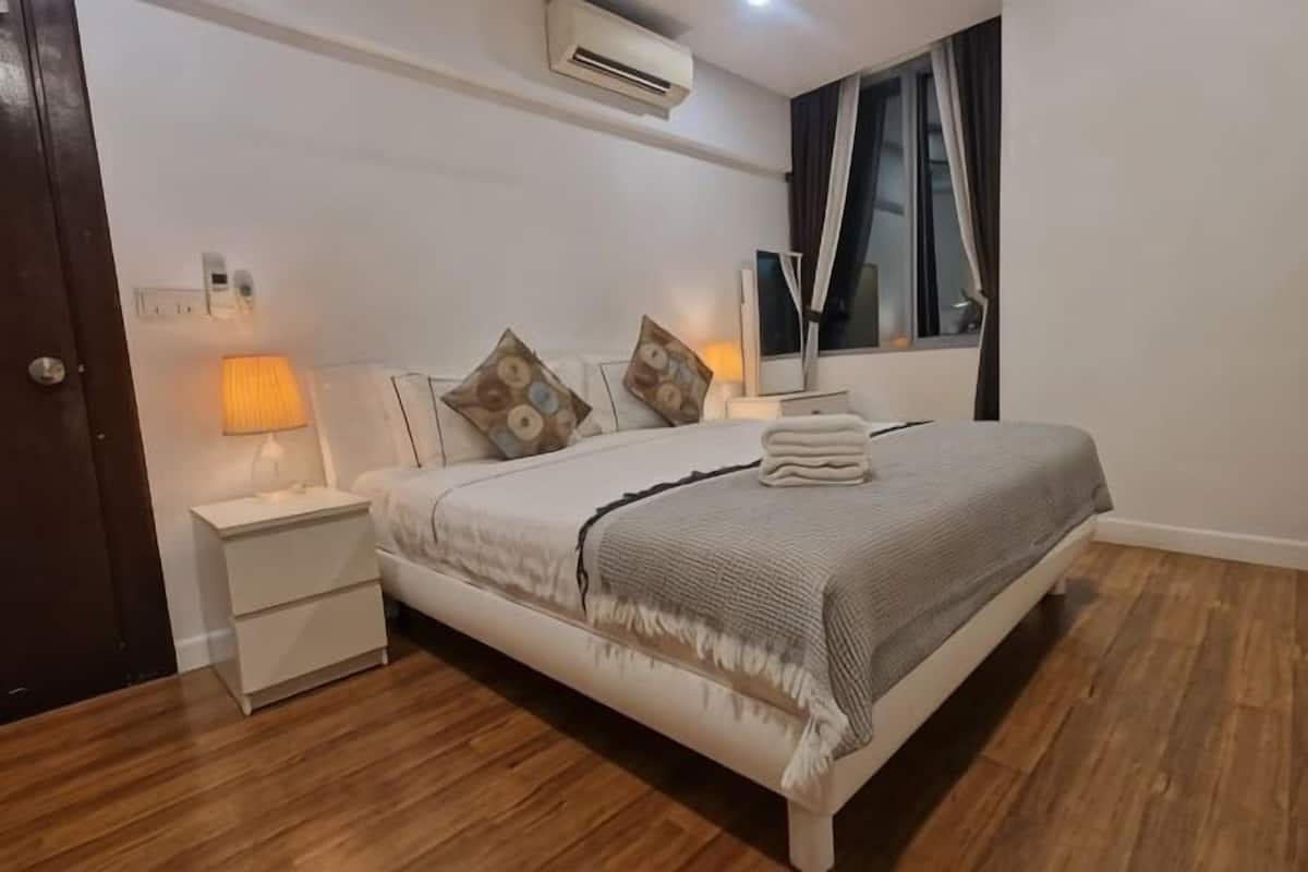 Une chambre à coucher comprenant un lit, des tables de chevet, une lampe, une fenêtre avec des rideaux et un appareil de climatisation.