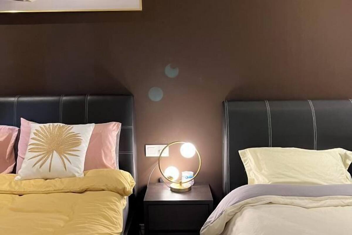 Un dormitorio con dos camas, una mesita de noche con luz de aro y un aplique de pared.