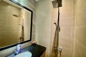 Un baño con lavamanos, espejo, ducha y paredes con azulejos.
