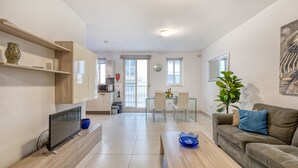Un salon moderne doté d’un téléviseur à écran plat, d’un canapé, d’une table basse et d’un coin repas avec des chaises et une table en verre.
