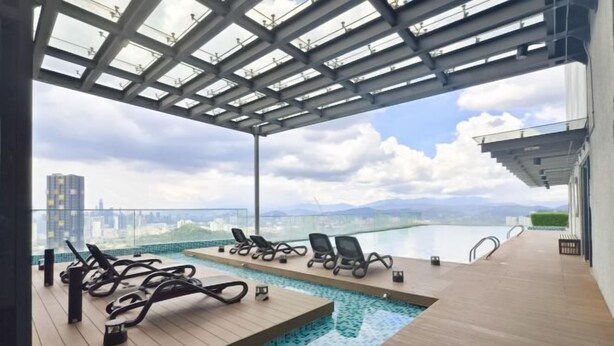 A rooftop infinity pool with lounge chairs and a wooden deck, overlooking a cityscape and mountains. - EkoCheras LumaStay (Kuala Lumpur)