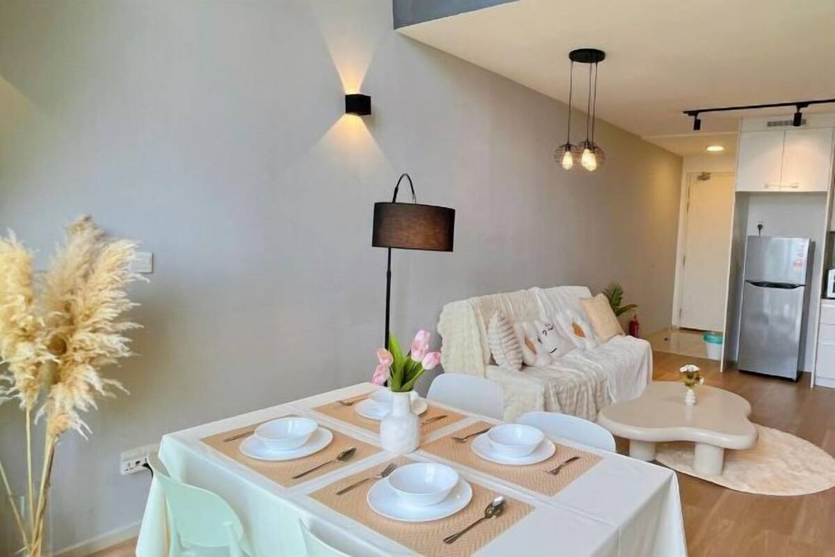 Un comedor moderno con una mesa preparada para cuatro, un sofá y una cocina al fondo.