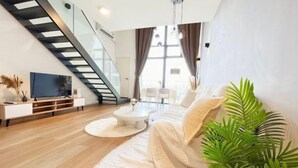 A modern living room with a staircase, a flat-screen TV, a round coffee table, and a large potted plant. - EkoCheras LumaStay (Kuala Lumpur)