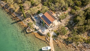 An aerial view of a coastal property with a house featuring a solar panel roof, a dock with a boat, and a clear view of the surrounding rocky shoreline and vegetation. - Villa Zora - Private Island Retreat (Sali)