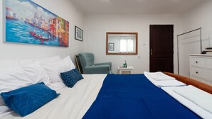 A hotel room with a bed, a chair, a desk, a wardrobe, and a painting of a cityscape. - Villa Zora - Private Island Retreat (Sali)