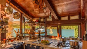 A rustic kitchen with wooden beams, a view of a lake, and various cooking utensils and pots. - Villa Zora - Private Island Retreat (Sali)