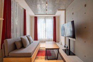 A modern living room with a sofa, a flat-screen TV, a coffee table, and a large window with curtains. - Leclerc Higashi-Shinjuku (Tokyo)
