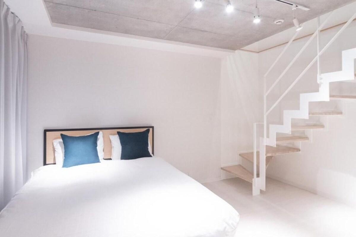 A modern bedroom with a large bed, a headboard, a staircase, and a white ceiling.