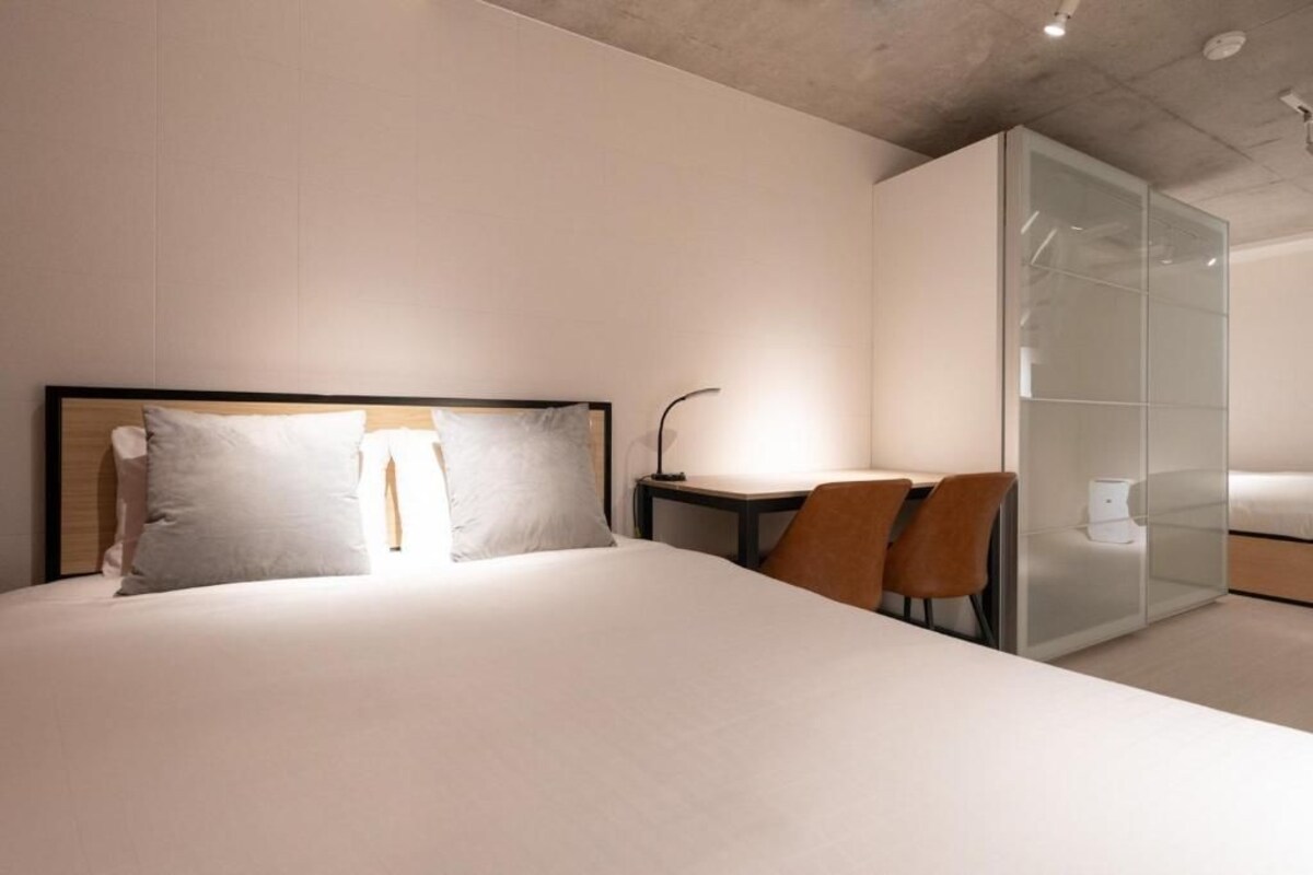 A modern hotel room with a bed, a desk, and a glass partition.