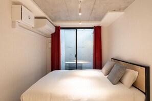 A hotel room with a bed, a ceiling fan, and a window with red curtains. - Leclerc Higashi-Shinjuku (Shinjuku)