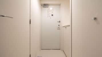 A narrow hallway with a white door at the end, a small sign on the floor, and a light switch on the wall.