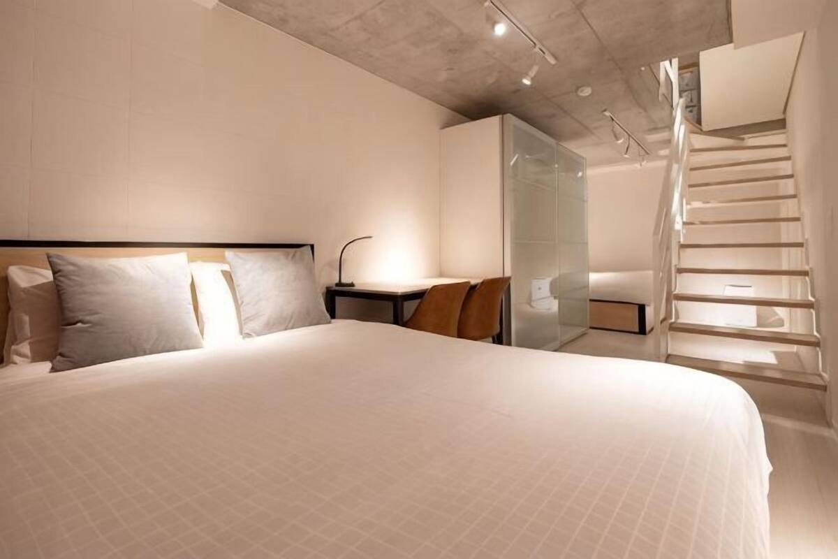 A modern hotel room with a large bed, a desk, and a glass-enclosed shower area.