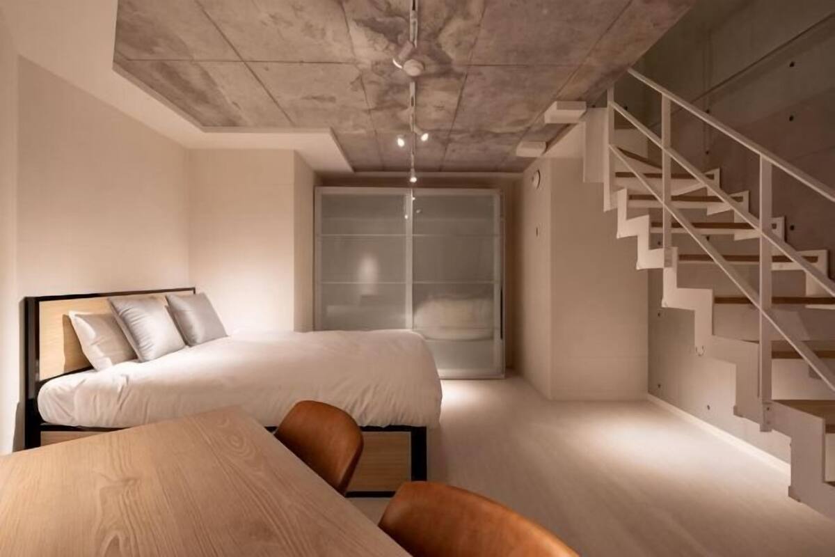 A bedroom with a bed, a desk, and a staircase.