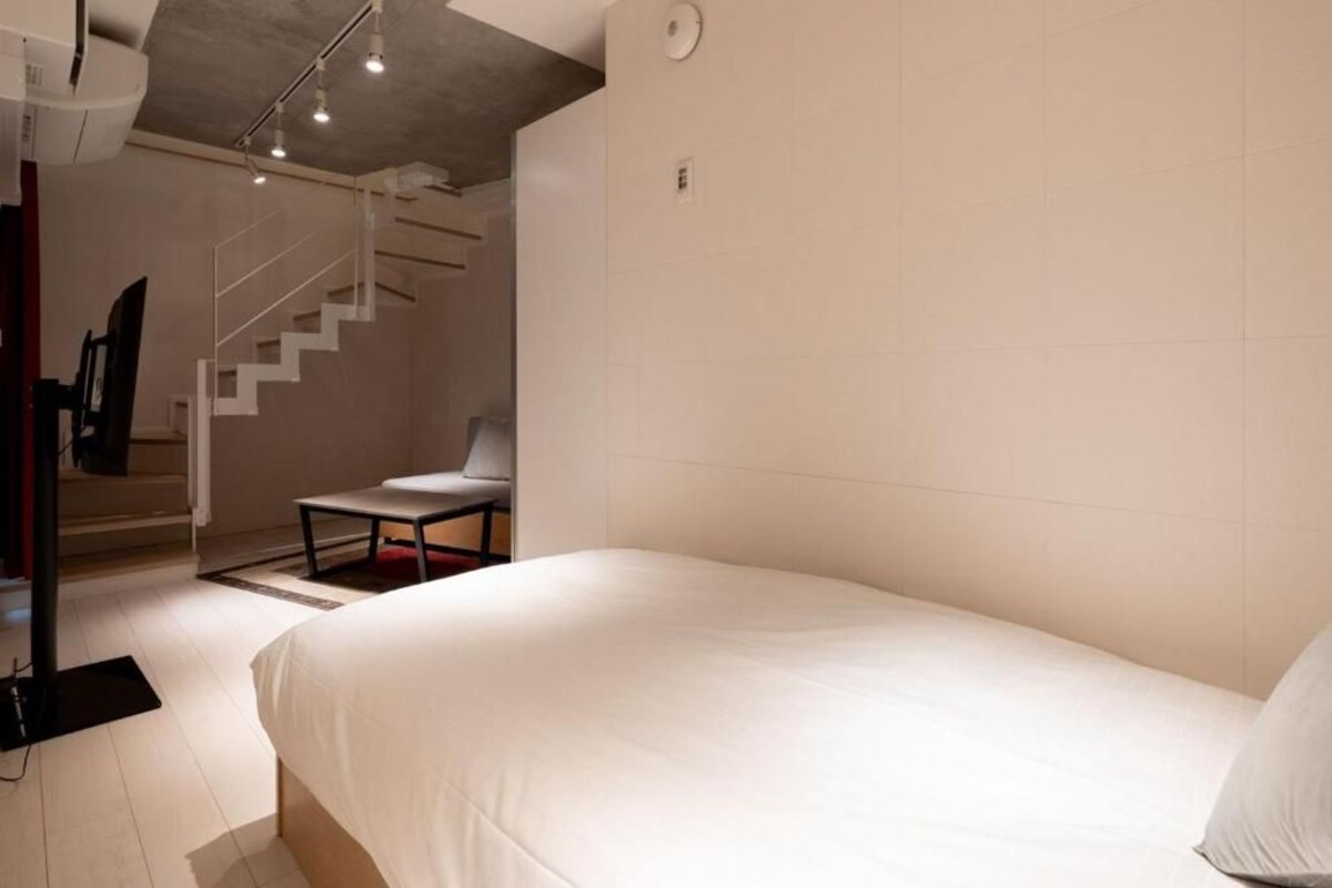 A hotel room with a bed, a chair, a desk, and a staircase.