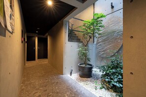 A hallway with a potted plant, a staircase, and a wall with a textured pattern. - Leclerc Higashi-Shinjuku (Shinjuku)