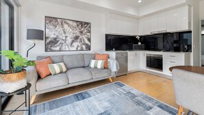 A modern living room with a grey sofa, a coffee table, and a large abstract painting on the wall. - Comfortable 2BR Retreat With Balcony & Parking (Melbourne)