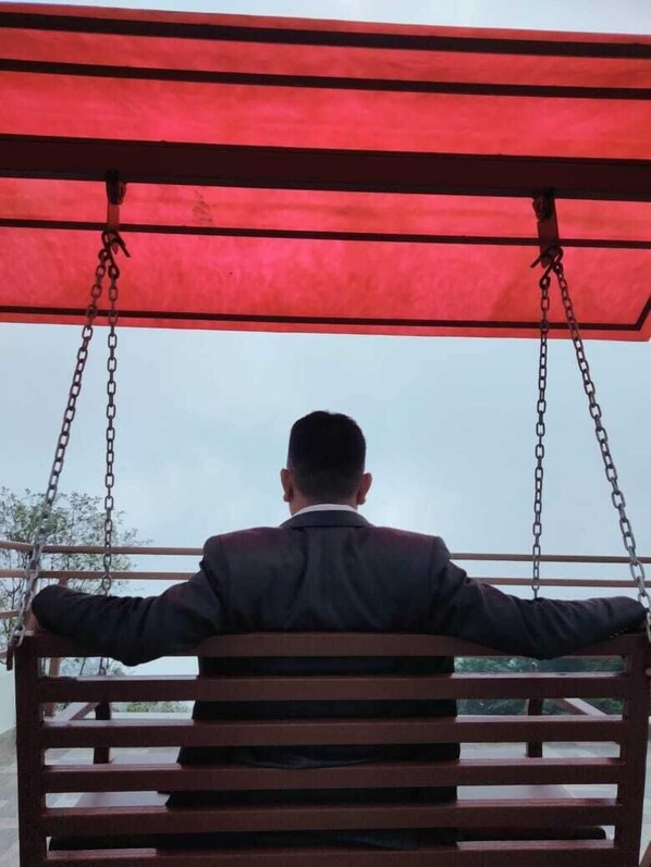 A person seated on a swing with a red canopy, facing away from the camera. - Hotel Himalayan Glacier (Baluwapati Deupur)