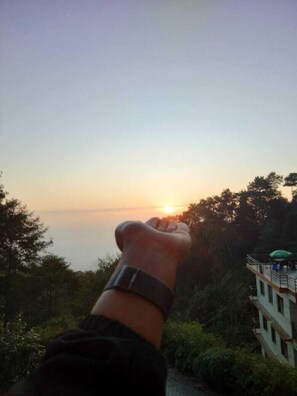 A hand with a watch, overlooking a building with a balcony and trees. - Hotel Himalayan Glacier (Baluwapati Deupur)