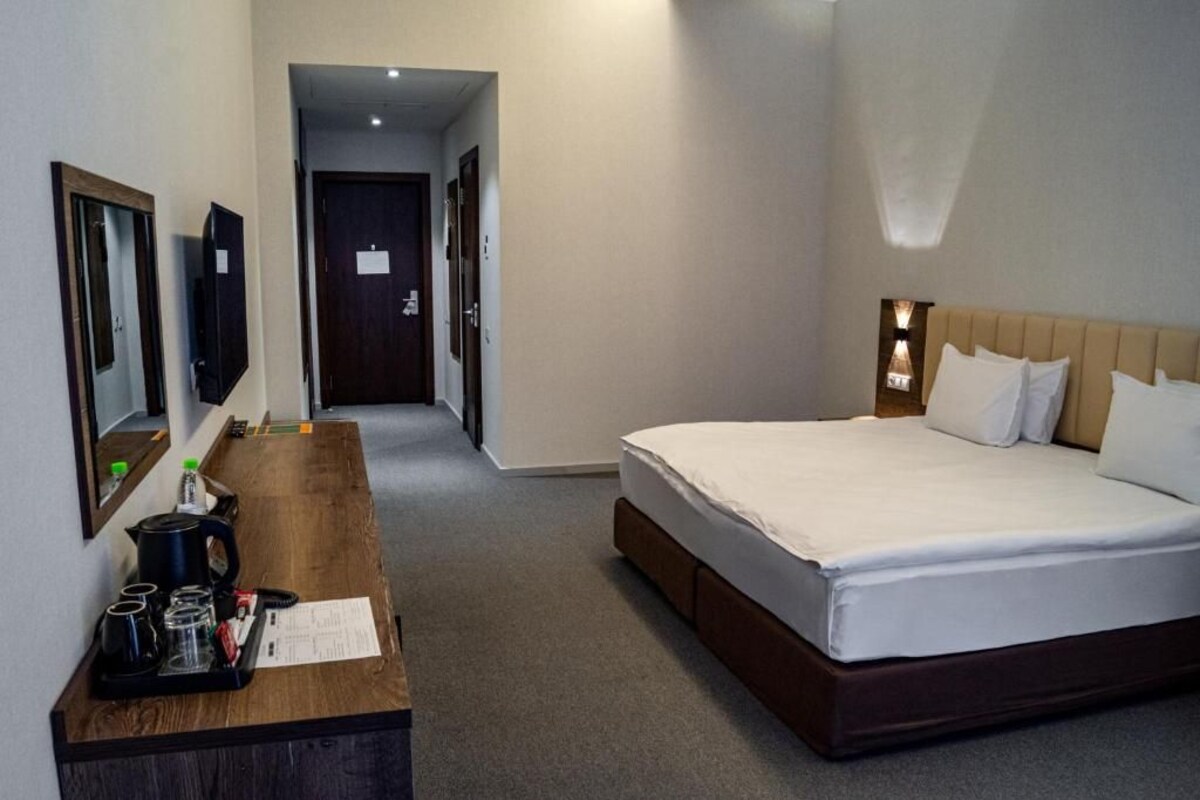 A hotel room with a bed, a wooden desk with a tray of items, a television, and a door leading to another room.