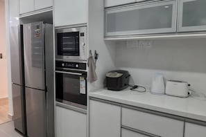 A kitchen with a refrigerator, microwave, oven, and a countertop with a toaster and kettle. - 3R@7pax++ Spacious Space Putrajaya. (Putrajaya)