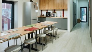 A modern kitchen with wooden cabinets, a stainless steel refrigerator, and a long dining table with stools.