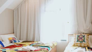 Un dormitorio con techo inclinado, una cama con colcha colorida, una mesita de noche con lámpara y cortinas traslúcidas.