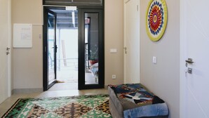 A hallway with a door leading to a balcony, a small bench, and a colorful wall decoration.