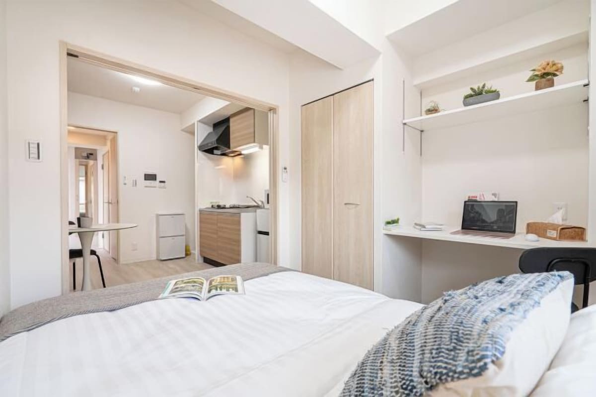 Ett modernt hotellrum med en säng, ett skrivbord, ett litet kök och ett badrum.