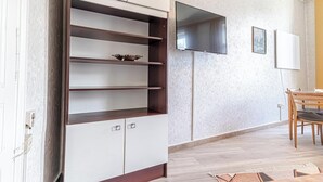 Ein Zimmer mit einem weißen Schrank mit mehreren Regalen, einem flachbildfernseher an der Wand und einem Holzespeisetisch mit Stühlen.