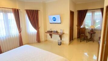 A hotel room with a bed, a desk with a lamp, a TV, and a trash bin.