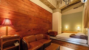 Une pièce aux murs lambrissés, avec un canapé en cuir, une table de chevet avec une lampe, un lit doté d’une tête de lit et une petite armoire en bois.
