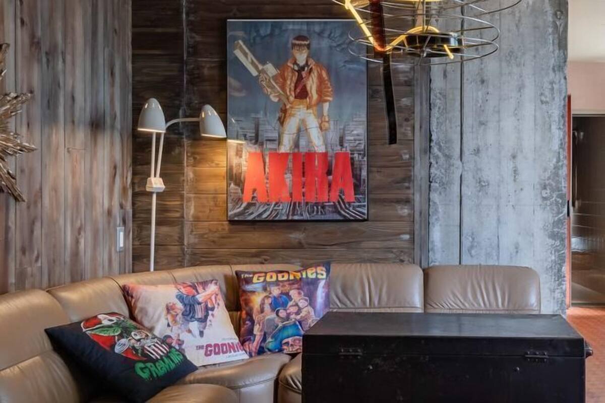 Une pièce avec un mur en bois, une affiche d’« Akira », un canapé en cuir agrémenté de coussins sur le thème de « Godzilla », et un meuble noir.