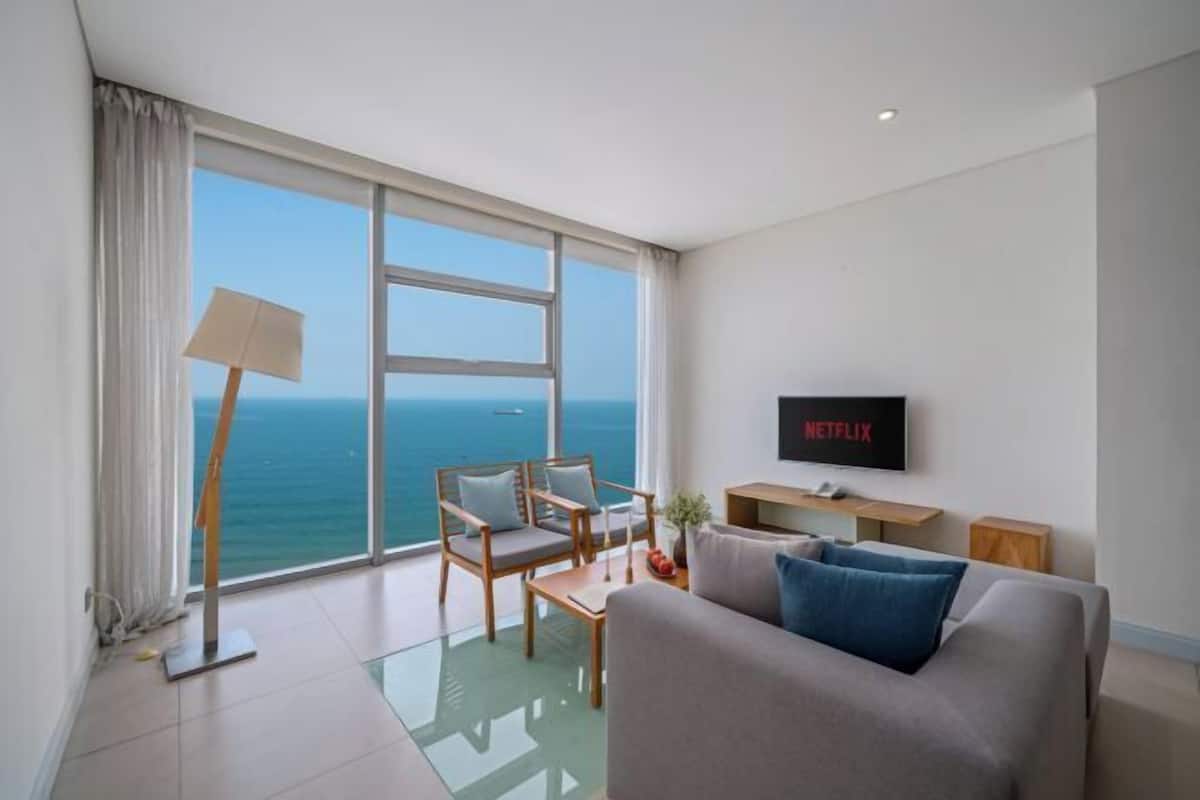 A modern living room with a large window, a sofa, a chair, a coffee table, a TV, and a lamp.