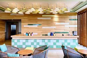 Een hotellobby met een receptiebalie, rieten stoelen en hanglampen.