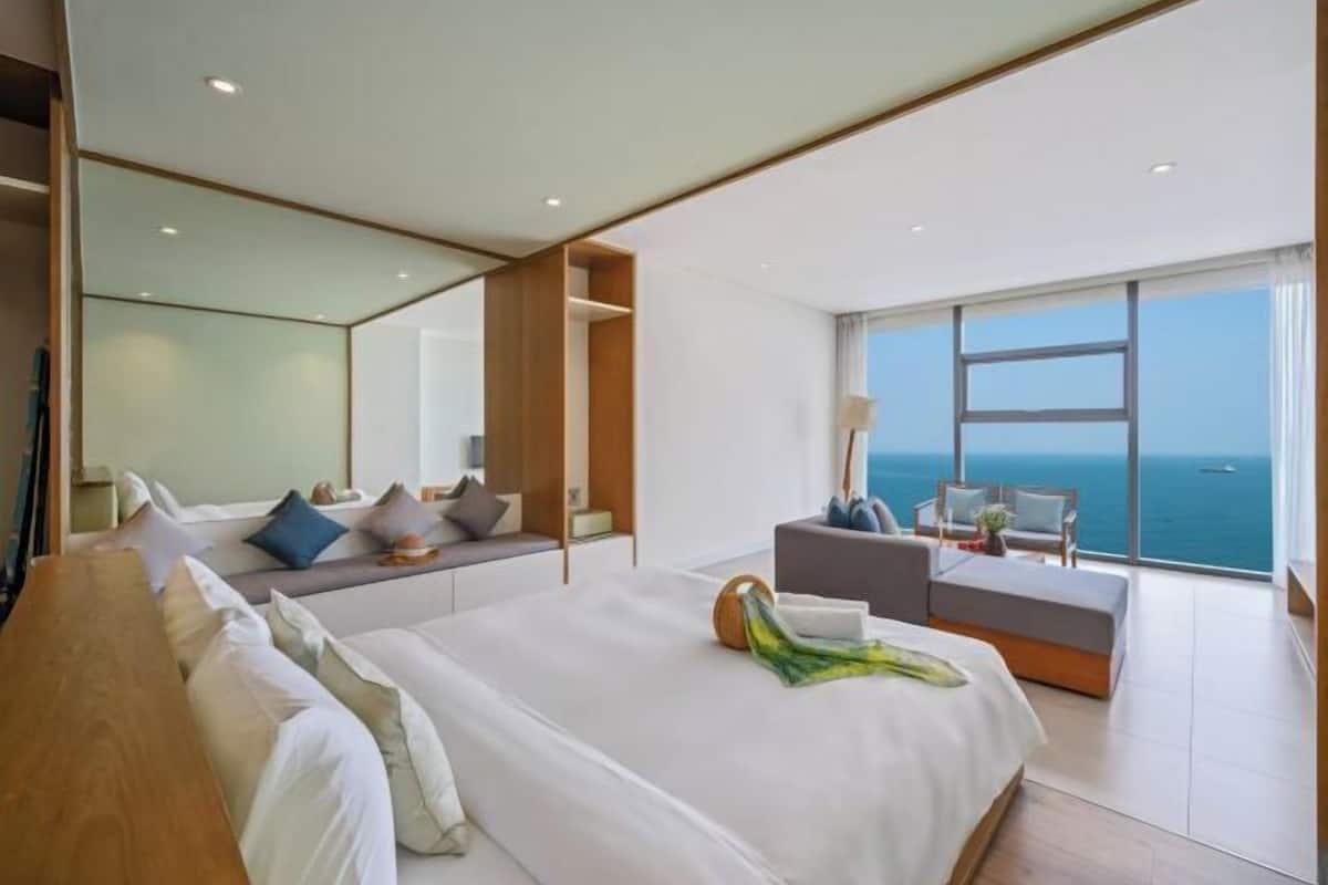 A modern hotel room with a large bed, a seating area, and a view of the ocean.