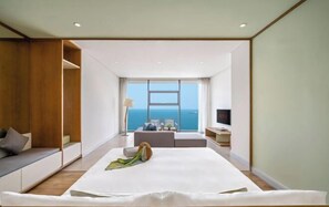 A modern hotel room with a large bed, a seating area, and a view of the sea.