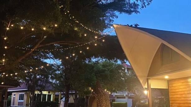 Un espace extérieur accueillant, agrémenté de guirlandes lumineuses, d’un grand parasol et d’un bâtiment à l’extérieur en bois.