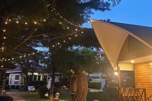 Un'area esterna accogliente con luci a tendina, un ombrellone grande e un edificio con facciata in legno.
