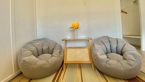 Une pièce avec deux fauteuils en forme de poire de couleur grise, une petite table en bois sur laquelle est posé un vase de fleurs, et un tapis rayé sur le sol.