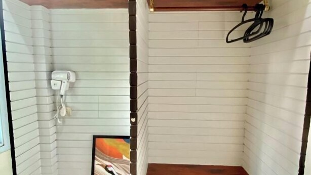 Rincón de una habitación con paredes blancas con paneles, suelo de madera y un secador blanco en la pared.
